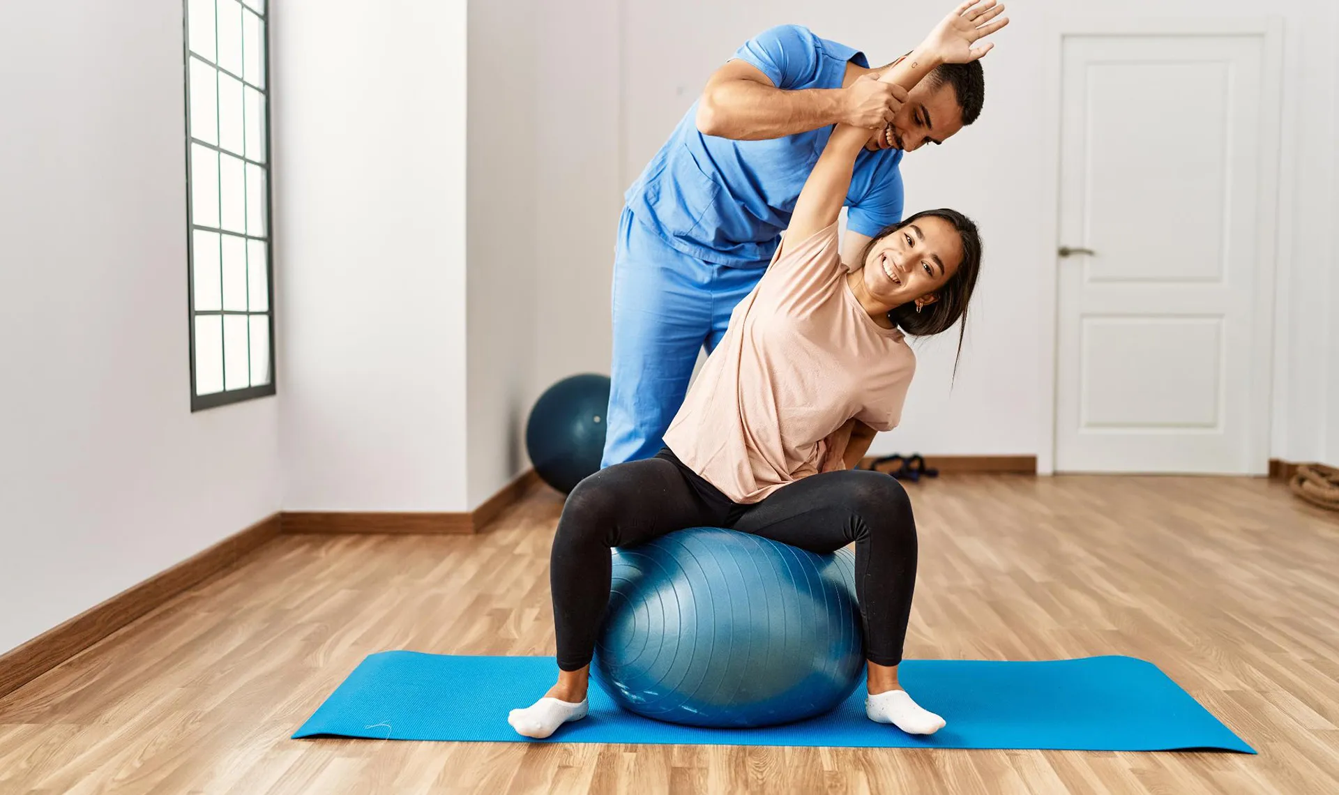 Bewegungstherapie im Reha-Zentrum Bad Ischl – Physiotherapeut unterstützt Patientin bei Dehnübung auf Gymnastikball